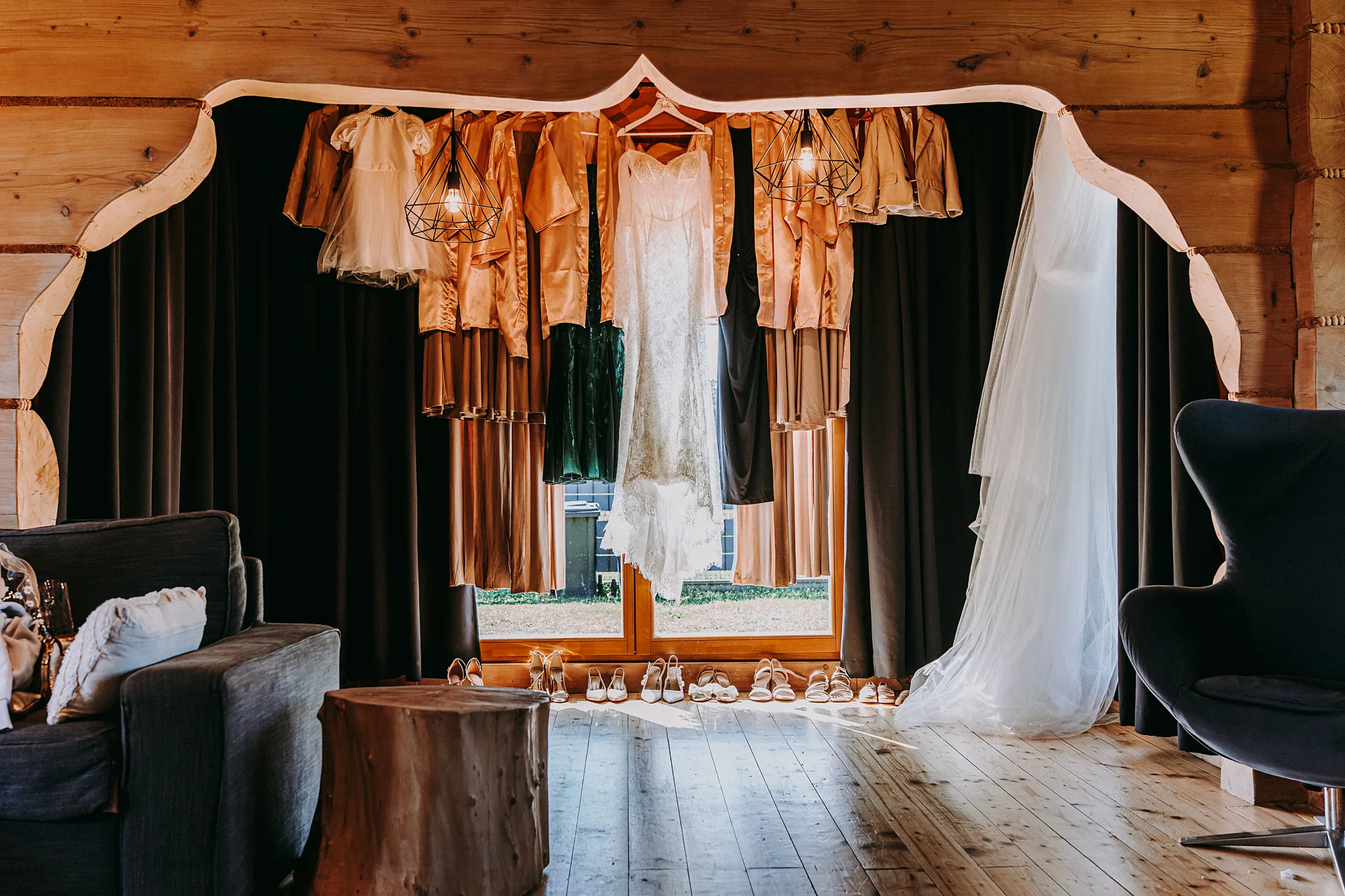 Koronkowa suknia ślubna zawieszona na tle drewnianej ściany domku w Zatoce Bajka, uchwycona przez Studio Grygierczyk.