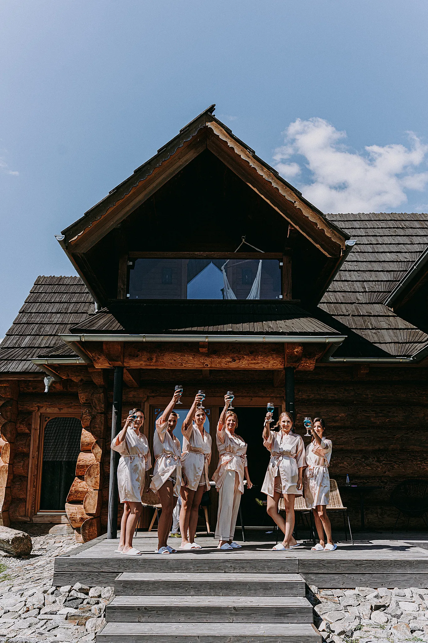 Druhny i panna młoda w szlafrokach wznoszą toast szampanem na tarasie domku w Hotelu Bajka