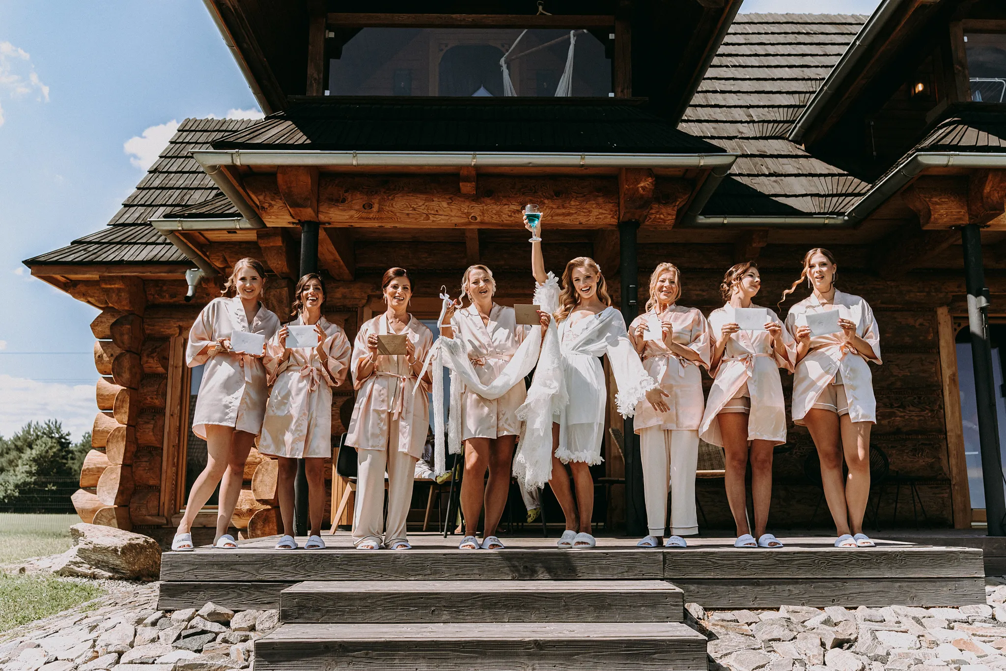 Druhny i panna młoda w szlafrokach wznoszą toast szampanem na tarasie domku w Hotelu Bajka.
