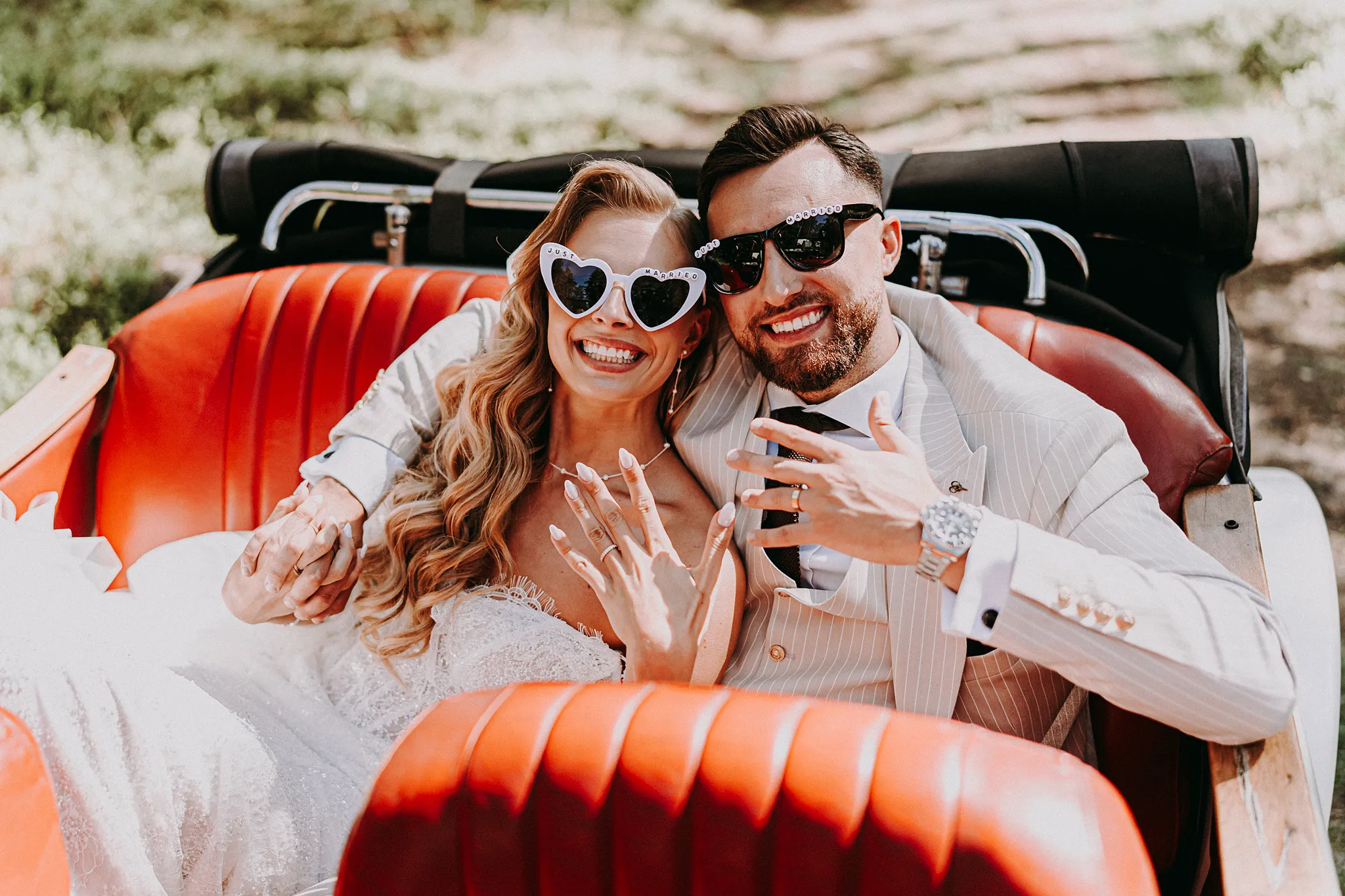 śmiechnięta panna młoda w stylowych okularach przeciwsłonecznych, trzymająca bukiet przy klasycznym aucie – fot. Studio Grygierczyk