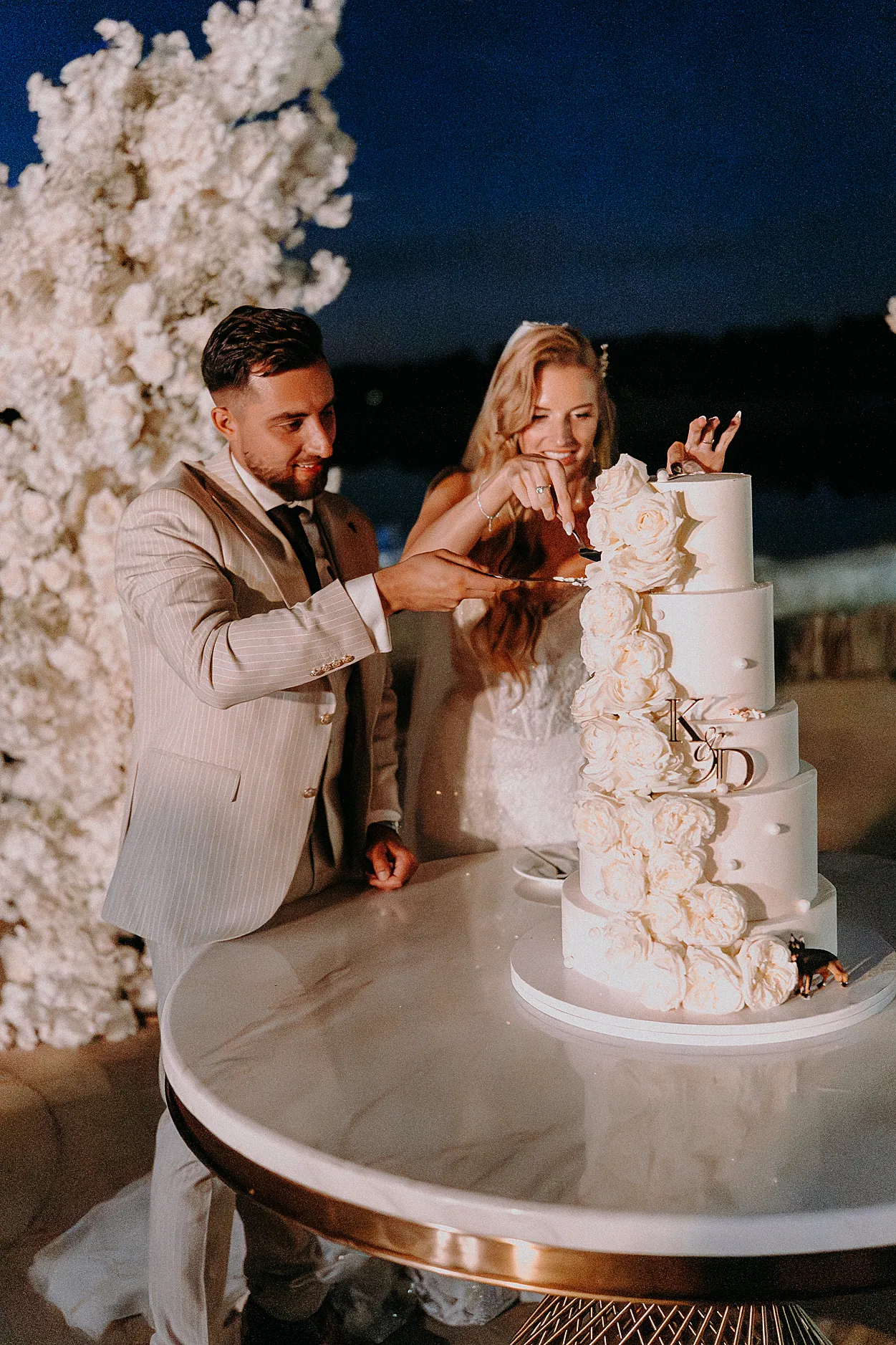 Krojenie tortu ślubnego nad jeziorem; światła fajerwerków i fontann iskier odbijające się w tafli wody w Grodźcu