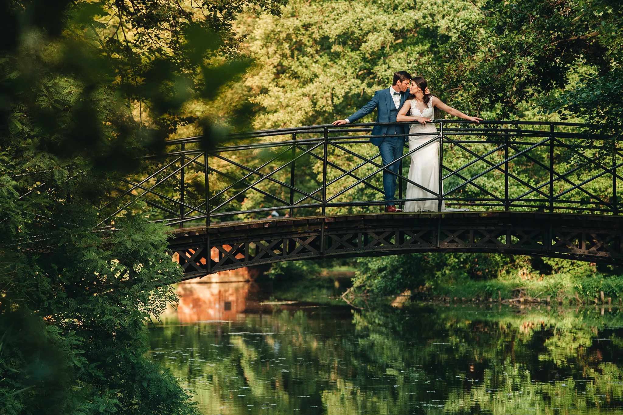 mloda para w oddali stoi na mosciie wsrod zieleni w romantycznym uscisku na tele zachodzacego slonca . park w pszczynie