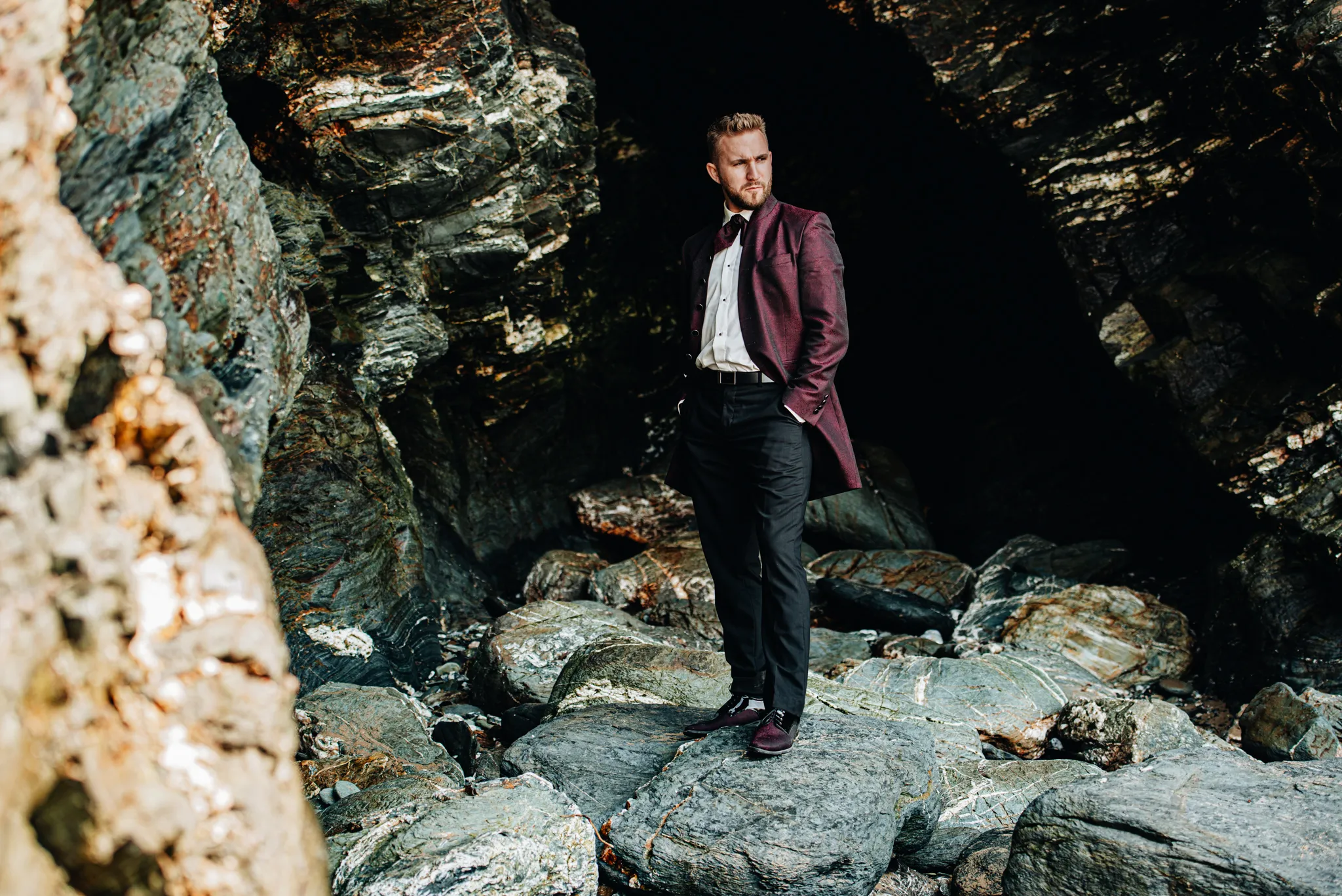 pan mlody stojacy na skalach na wybrzerzu kornwali przy oceanie ubrany w wisniowy surdut