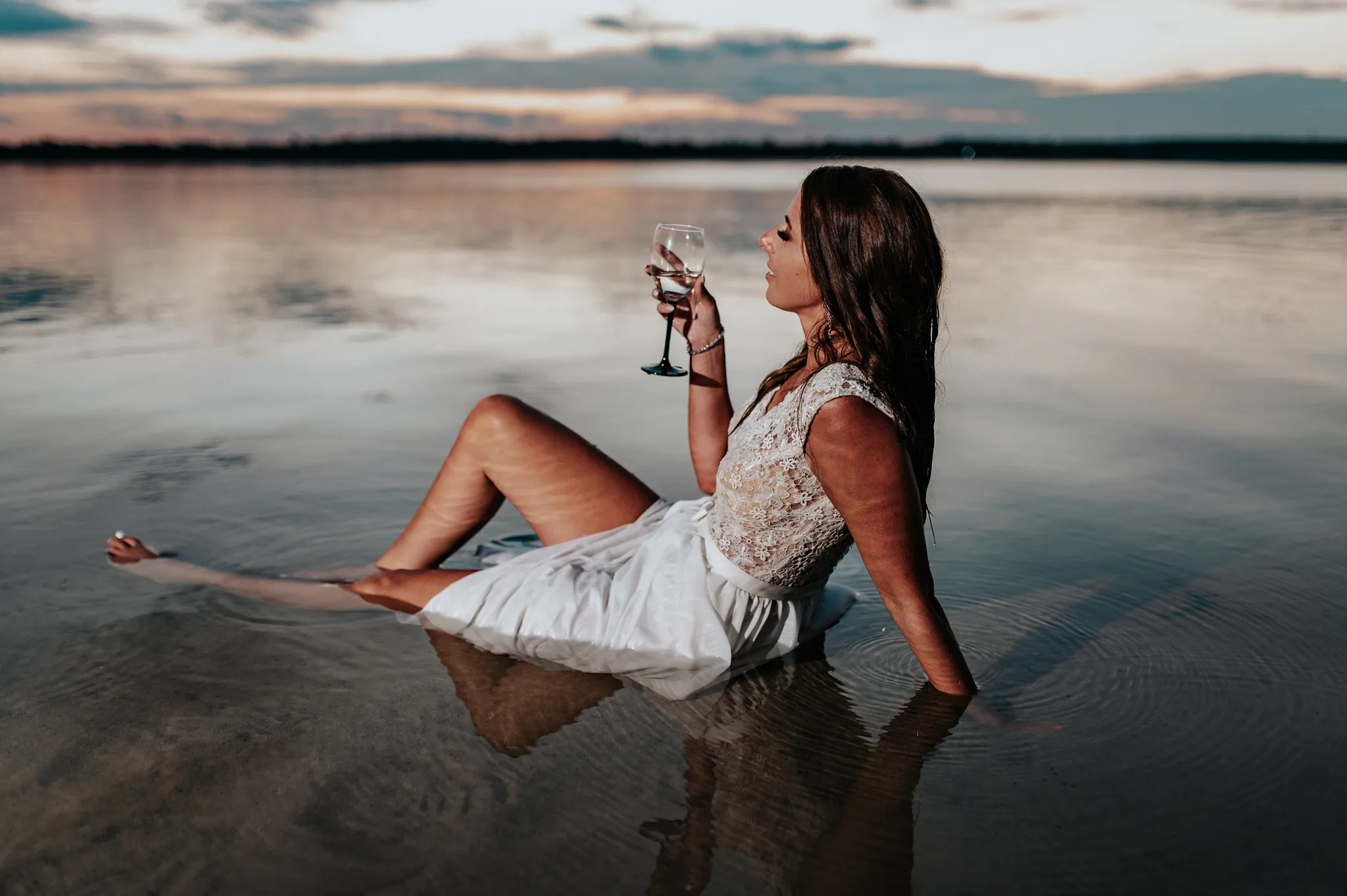 mloda pani w koronkowej sukience siedzaca w cieplej wodzie nad jeziorem z kieliszkiem szampana chilluje
