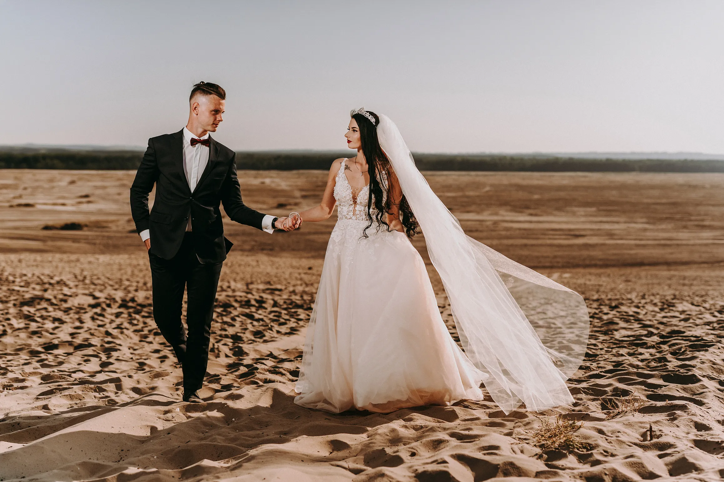 para mloda spacerujaca po pustyni w cieplym kolorze swiatla. pani mloda z dlugim welonem, niepozowane-zdjecia-slubne-studio-grygierczyk